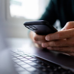 Person using a smartphone next to a laptop, representing digital communication for businesses in Dubai and the UAE.