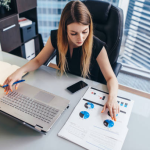 A businesswoman reviews documents and data at her desk, preparing to meet UAE company naming requirements.