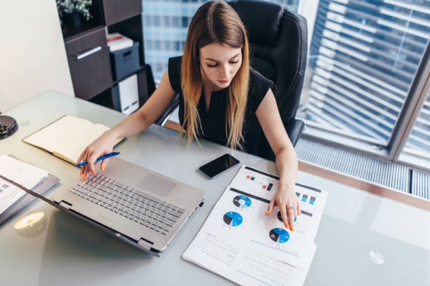 A businesswoman reviews documents and data at her desk, preparing to meet UAE company naming requirements.