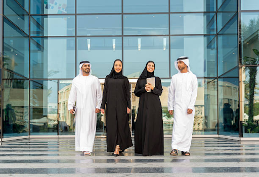 Group of professionals in traditional attire walking outside a modern glass building, illustrating UAE business culture.