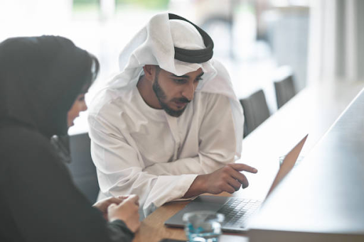 Two professionals in traditional attire discussing business over a laptop, indicative of UAE free zones.